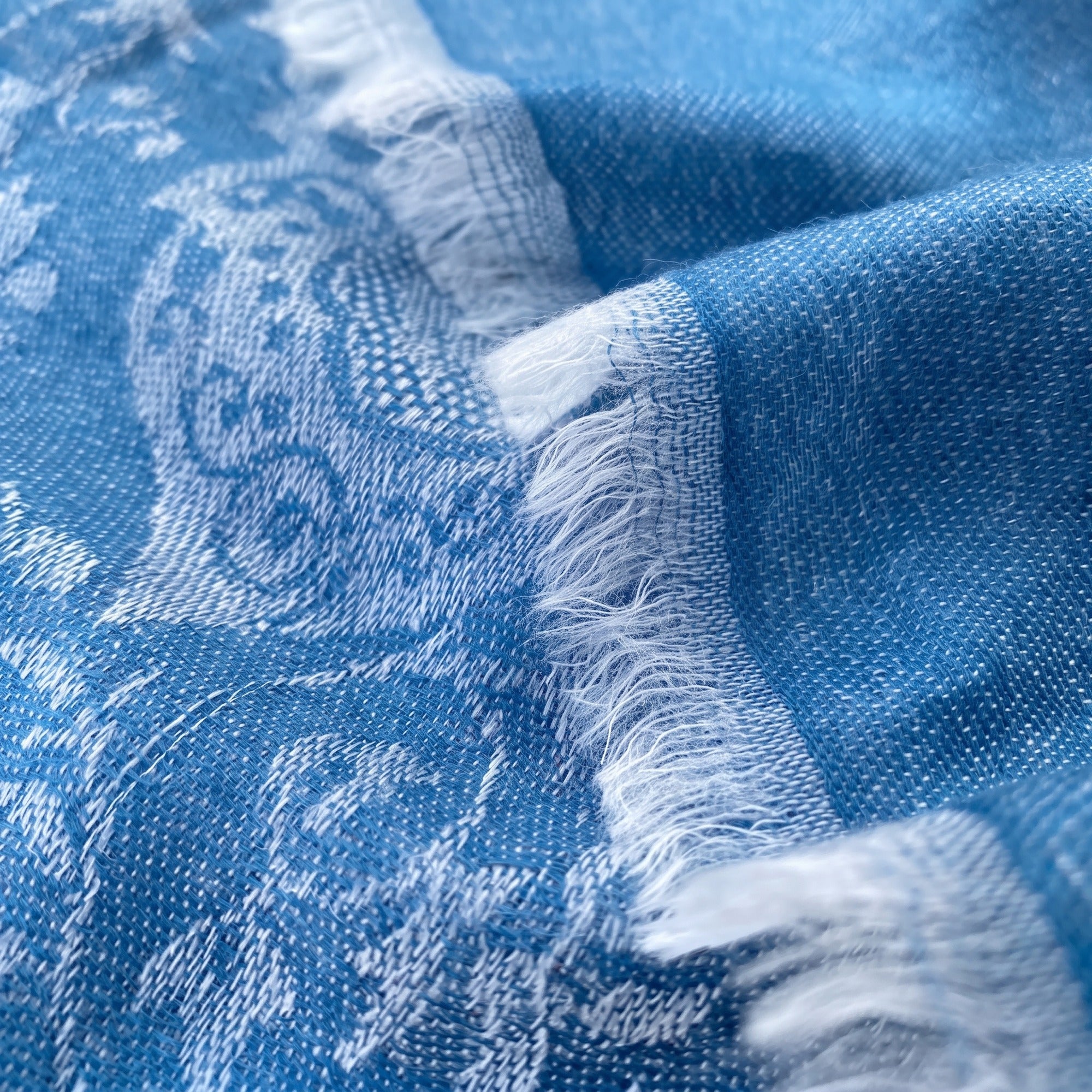 Nahaufnahme eines handgewebten Kaschmirtuchs in Blau mit eingewebtem Paisleymuster und weißen Fransen