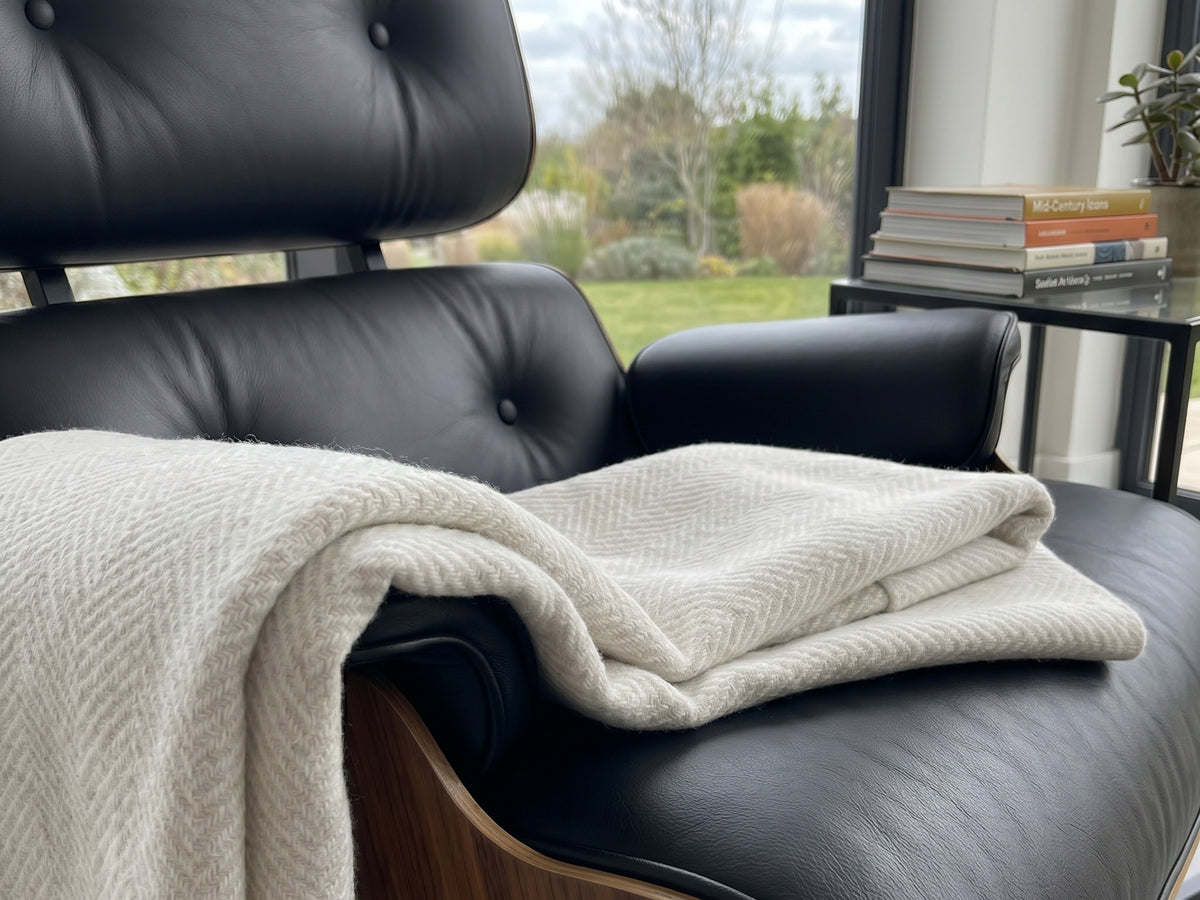 Cremefarbene Kaschmirdecke über einem Ledersessel am Fenster